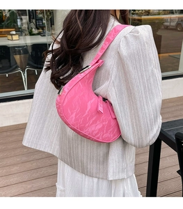 Pink patent leather crescent shoulder bag styled on a wooden patio outdoor setting