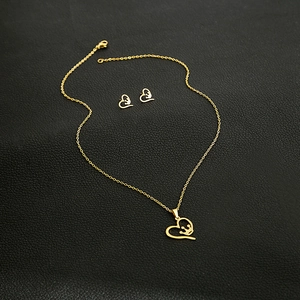 Detail of heart crown necklace and earrings set in gold finish on black background