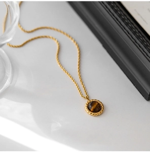 Macro detail of round tiger eye pendant with twisted gold rope border and matching chain