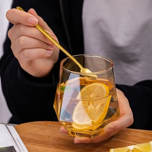 Amber hexagon glass cup with diamond faceted design held by hand on wooden table