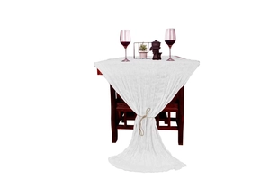 Close-up of white wrinkled cheesecloth table runner draped elegantly over a wooden table
