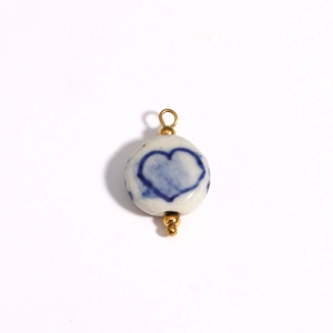 Detailed shot of a round white ceramic pendant with blue heart print and 18K gold ring