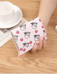 Pink PU leather wallet with cute cow and strawberry prints held over a wooden table