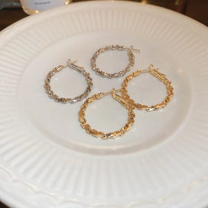 Close-up of gold and silver irregular geometric hoop earrings on a white textured dish