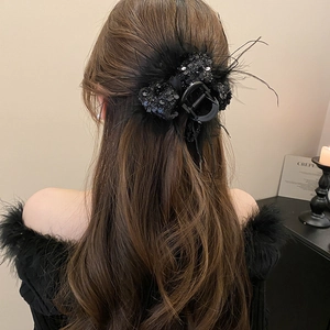 Detail of a large black hair claw clip with feathers and sequins on long wavy hair