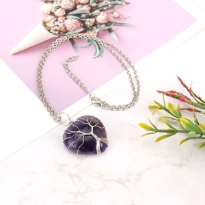 Detail of silver wire-wrapped tree of life purple stone heart pendant on marble background
