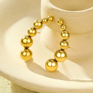 Golden C-shaped titanium steel bead earrings with gradient beads on beige ceramic surface