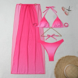 Flat lay of pink gradient bikini set with mesh sarong and gold chain detail on beach sand