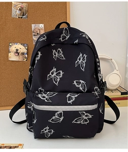 Detail of black backpack with silver butterfly print on desk with school accessories