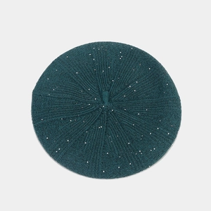 Detailed top view of dark green sequined knit beret with ribbed texture on gray surface