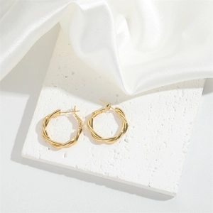 Close-up of golden twisted rope hoop earrings on a textured white stone tile