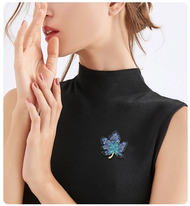 Detail view of a luxury blue and green rhinestone maple leaf brooch on a black garment