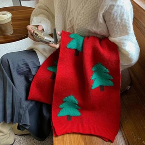 Knitted Christmas scarf with red base and green tree patterns in a cozy winter setting
