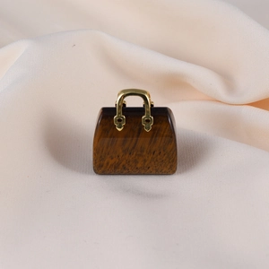 Macro shot of a handbag-shaped quartz stone pendant with gold handle on beige fabric