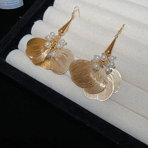 Detail of gold flower tassel earrings with layered metal petals and pearl clusters