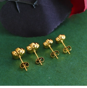 Macro shot of gold vintage rose stud earrings on a green textured surface with petals