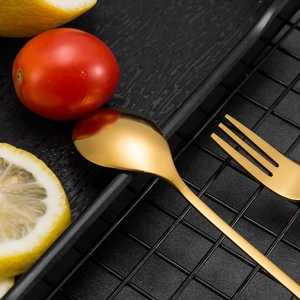 Golden stainless steel spoon and fork set with leaf handles on a stylish black tray