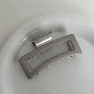Detail shot of a silver metal shark hair claw clip with a hollow square design on a white dish