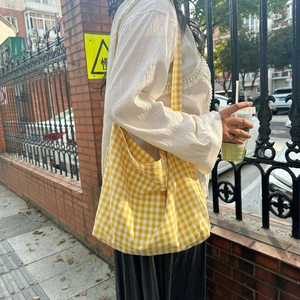 Outdoor shot of a yellow plaid canvas tote bag with a minimalist tag and long shoulder strap