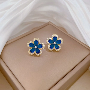 Detailed close-up of gold flower stud earrings with blue gemstone and micro-inlaid crystals