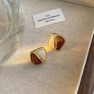 Close-up of geometric triangle drop earrings with amber and cream resin in gold frame