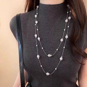 Double-layered long necklace with baroque pearls and silver beads on a gray sweater