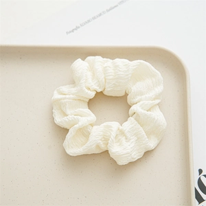Detailed view of off-white pleated polyester scrunchie on a decorative ceramic tray