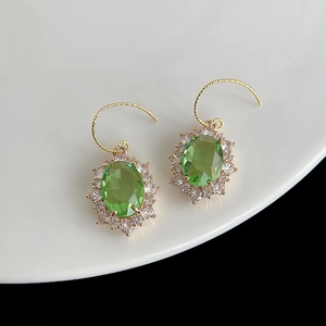 Détail de boucles d'oreilles fleur en plaqué or avec zircon vert sur une assiette blanche
