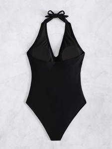 Flat lay of black one-piece swimsuit with halter neck and bow detail on marble background