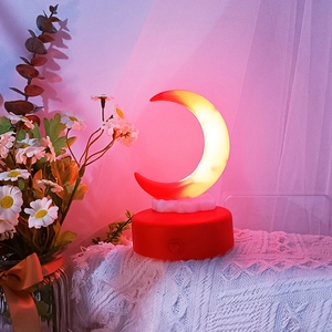 Detail of moon-shaped night light with red and yellow gradient on a cozy bedside table