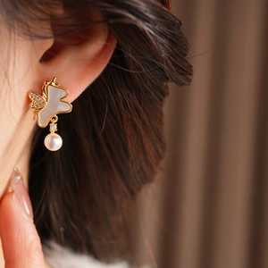 Détail d'une boucle d'oreille papillon en or 18k avec nacre, cristaux et perle blanche ronde