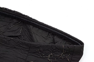 Detailed close-up of black pleated fabric with gold metallic thread and textured waist design