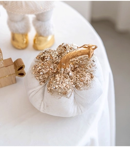 Close-up of a white velvet pumpkin with gold sequins and a curved metallic stem decoration