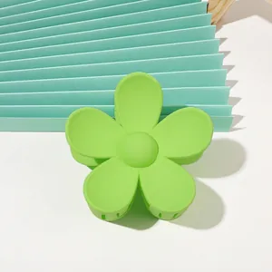 Detail of green matte flower hair claw clip with minimalist five-petal design on desk