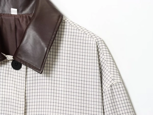 Détail de la veste à carreaux noir et blanc avec col en cuir marron et boutons noirs