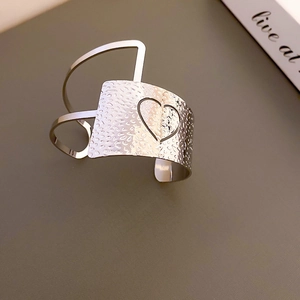 Detail of silver drop cuff bracelet featuring hammered metal texture and heart cutout