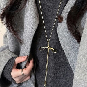Elegant gold bow pendant necklace with long tassels on a model wearing a grey coat
