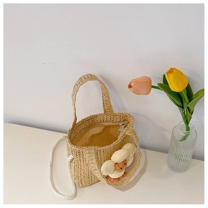 Detail view of a beige straw handbag for children with a large fabric flower and zipper