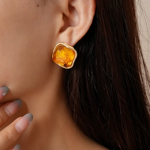 Gros plan de boucles d'oreilles carrées en résine ambre et or sur le modèle