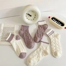 Detailed macro view of cream and purple cable knit socks with assorted ribbed textures