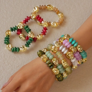 Detail view of colorful acrylic beaded bracelets with irregular gold metal accents on a model