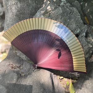 Classical gradient gold and dark red folding fan with hollow bamboo ribs on a rock