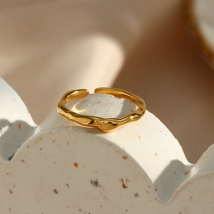 Close-up of golden irregular wavy ring on white ceramic stand with soft lighting
