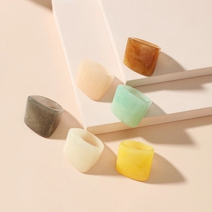 Set of minimalist square resin rings in multi-color earth tones on a stone platform