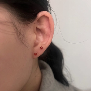 Close-up of minimalist red bead stud earrings worn on ear with small round 4mm design