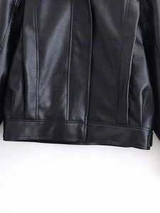 Close-up of black PU leather jacket showing detailed lychee grain texture and finish