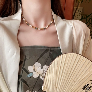 Detailed view of multi-colored beaded necklace on model with traditional folding fan