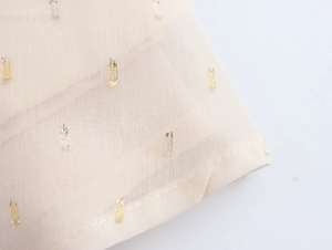 Macro shot of beige chiffon fabric detail with metallic gold sequins on the sleeve
