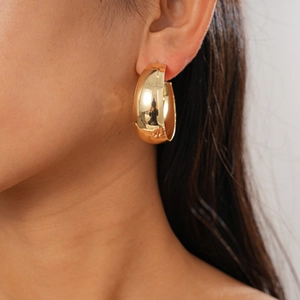 Close-up of chunky gold-plated C-shaped hoop earrings on a model with metallic finish