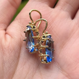 Vista detallada de pendientes vintage dorados con piedras azules óvalas en mano